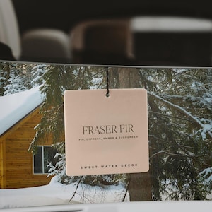 May include: A beige car air freshener with the text "Fraser Fir" and "Fir, Cypress, Amber & Evergreen" in brown text. The text "Sweet Water Decor" is also in brown text at the bottom of the air freshener.