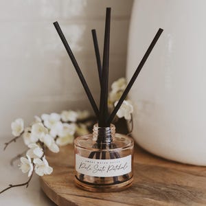 May include: A clear glass bottle diffuser with black reeds and a label that reads "Sweet Water Scents Palo Santo Patchouli".