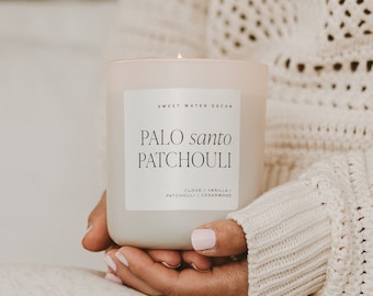 May include: A white candle with a label that reads "Sweet Water Decor Palo Santo Patchouli Clove / Vanilla / Patchouli / Cedarwood".