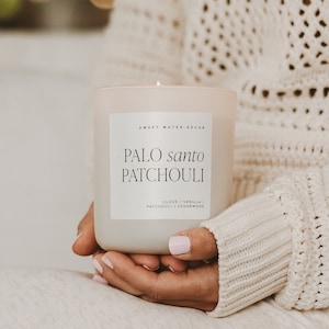 May include: A white candle with a label that reads "Sweet Water Decor Palo Santo Patchouli Clove / Vanilla / Patchouli / Cedarwood".