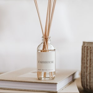 May include: A clear glass bottle with a white label that reads "FARMHOUSE SWEET WATER DECOR" and natural wooden sticks inside. The bottle is sitting on a stack of books.