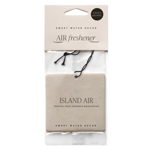 May include: An air freshener in a clear plastic package. The product is rectangular and beige, with the words "ISLAND AIR" and "TROPICAL FRUIT, ORANGE & MOUNTAIN AIR" printed on it. The packaging also includes the text "SWEET WATER DECOR" and "AIR freshener".