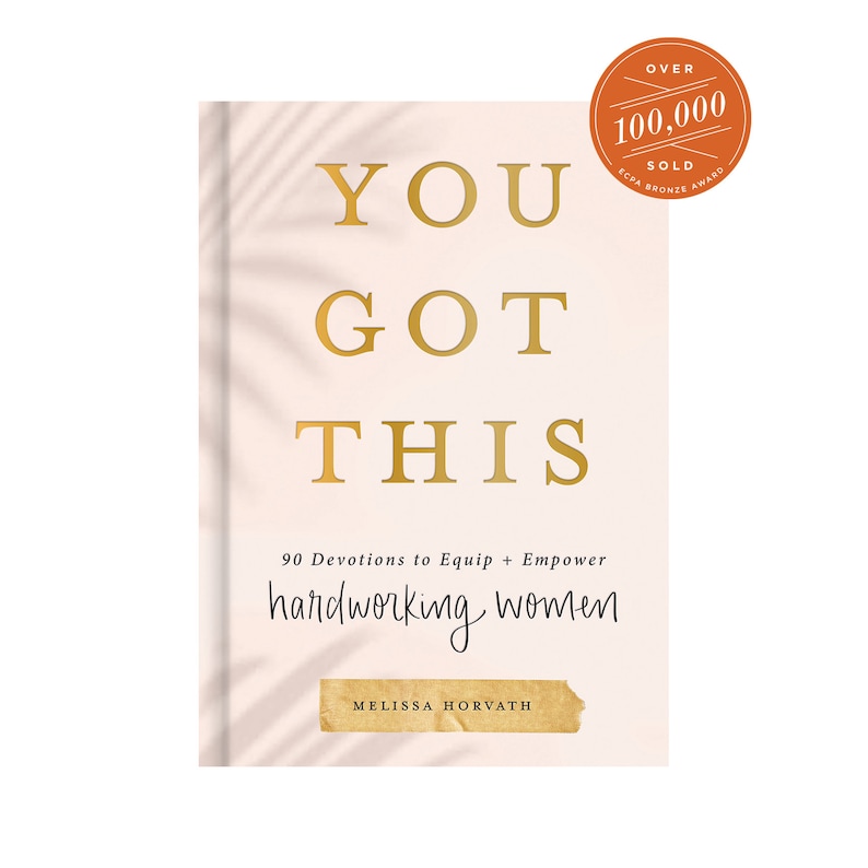 May include: A book cover with the title "YOU GOT THIS" in gold lettering. The subtitle is "90 Devotions to Equip + Empower hardworking women". The author's name, "MELISSA HORVATH", is printed in gold lettering on a brown rectangle at the bottom of the cover. The cover is a light pink color with a shadow pattern.