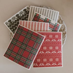 May include: A collection of rectangular cleaning cloths featuring various patterns including red and green plaid, red with white reindeer and snowflake motifs, black with white snowflake designs, and vertical stripes in red or black on white backgrounds.