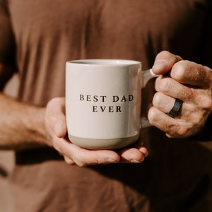 May include: A white ceramic mug with a brown rim and handle. The mug has the text "BEST DAD EVER" printed in black on the front.