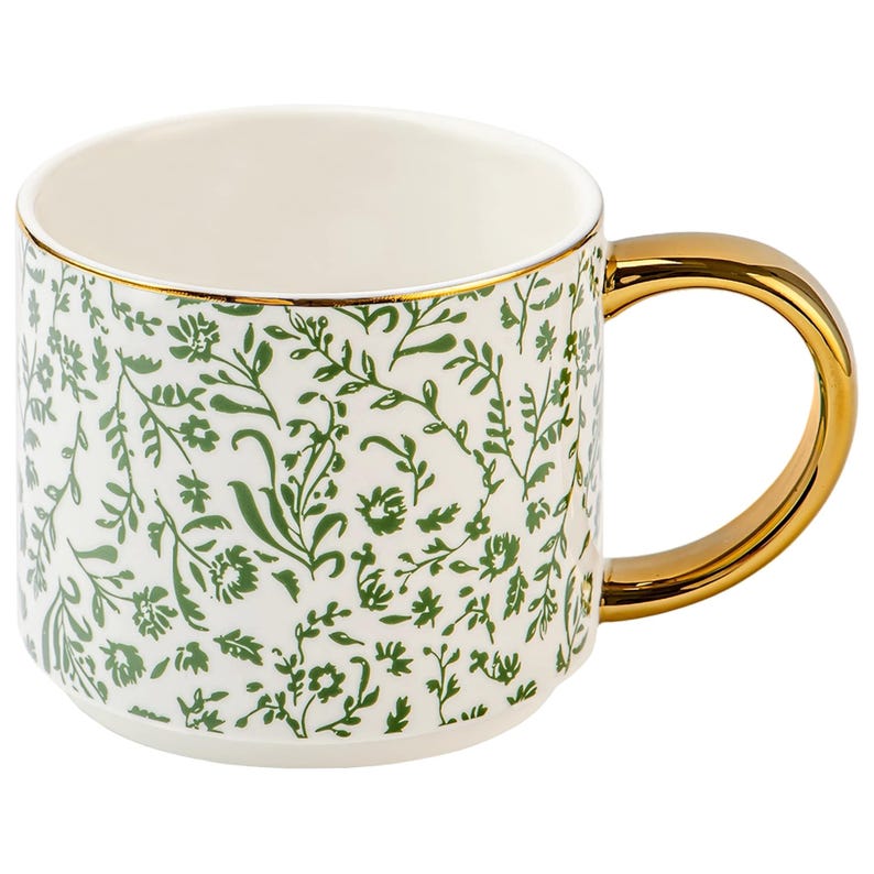 May include: White ceramic mug with a gold handle and rim. The mug is decorated with a green floral pattern. The handle is a solid gold color, and the rim has a thin gold band.