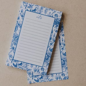 May include: Two blue and white floral patterned notepads with lined pages. The top notepad has the word "notes" written in cursive.