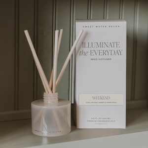 May include: A reed diffuser with a frosted glass bottle and light-colored reeds next to a white rectangular box labeled SWEET WATER DECOR, ILLUMINATE the EVERYDAY, REED DIFFUSER, WEEKEND, SAGE, ORANGE, AMBER & TONKA BEAN, 3.5 FL OZ (104 ML).