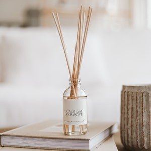 May include: A clear glass bottle diffuser with wooden sticks and a white label that reads "CALM and COMFORT SWEET WATER DECOR".