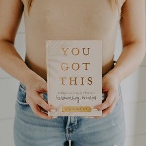 May include: A white book with gold lettering that reads "You Got This" and "90 Devotions to Equip + Empower hardworking women" by Melissa Horvath.
