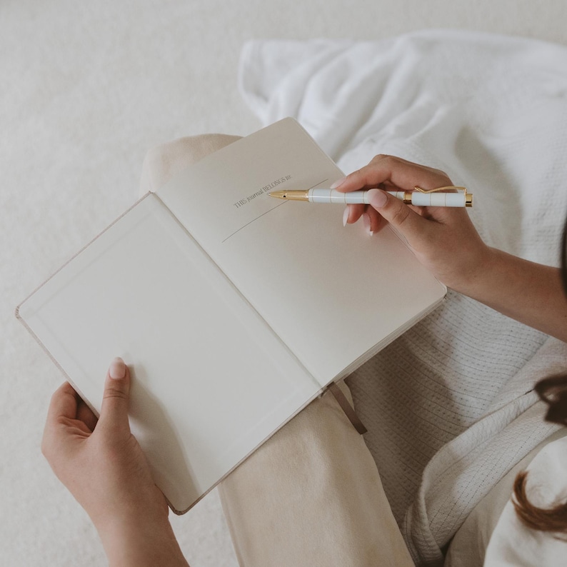 Pu&ograve; includere: Un diario bianco con una penna dorata sopra. Il diario ha il testo "THE MORNING GLORIFY" stampato sulla copertina.
