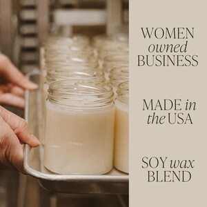 May include: A tray of clear glass jars filled with a white soy wax blend. The jars are arranged in rows and are being moved by a hand. The text "WOMEN owned BUSINESS MADE in the USA SOY wax BLEND" is visible on the right side of the image.