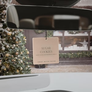 May include: A tan car air freshener with the text "Sugar Cookies" and the description "Sugar Cookies, Buttercream & Vanilla" and the brand "Sweet Water Decor".