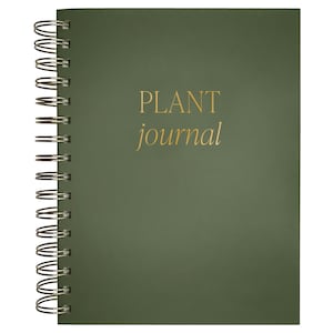 May include: A dark olive green spiral-bound journal with a metallic gold foil inscription on the front cover that reads PLANT journal in a combination of uppercase and lowercase serif lettering, featuring a silver-toned metal wire binding.