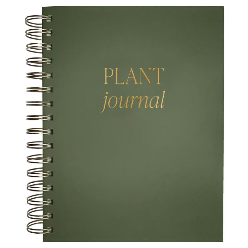 May include: A dark olive green spiral-bound journal with a metallic gold foil inscription on the front cover that reads PLANT journal in a combination of uppercase and lowercase serif lettering, featuring a silver-toned metal wire binding.