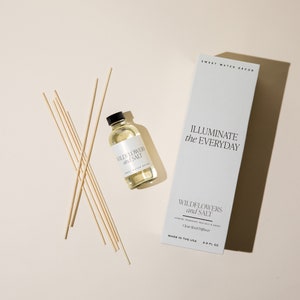 May include: A clear glass bottle of Wildflowers and Salt reed diffuser with a white label and a set of wooden diffuser sticks. The bottle is sitting on a light beige surface. The label reads "Wildflowers and Salt" and "Clear Reed Diffuser". The bottle is 3.5 fl oz and made in the USA.