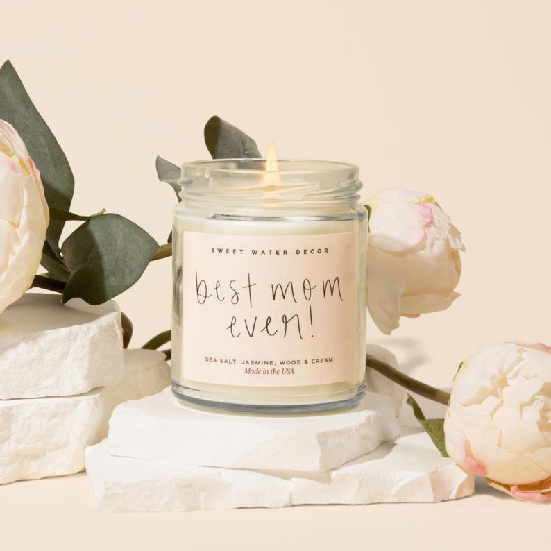 May include: A clear glass candle jar with a white label that reads "SWEET WATER DECOR best mom ever! SEA SALT, JASMINE, WOOD & CREAM Made in the USA".