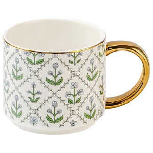 May include: A white ceramic mug with a gold handle and rim. The mug features a repeating pattern of green leaves and blue flowers on a white background. The mug is designed for hot beverages.
