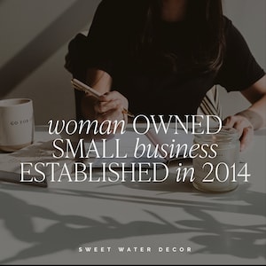 May include: A person writing with a pen on a desk with a mug that says "GO FOR IT". The text on the image reads "woman OWNED SMALL business ESTABLISHED in 2014". A lit candle sits on the desk.