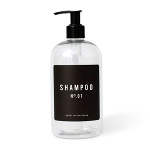 K&ouml;nnte beinhalten: Transparente Plastik-Pumpflasche mit einem schwarzen Etikett, auf dem "SHAMPOO N&deg;01" und "SWEET WATER DECOR" steht.