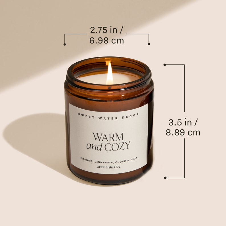 Peut inclure: Un bocal en verre brun contenant une bougie avec une &eacute;tiquette blanche sur laquelle est inscrit "SWEET WATER DECOR WARM and COZY ORANGE. CINNAMON. CLOVE & PINE Made in the USA". La bougie est allum&eacute;e et le bocal mesure 8,89 cm de haut et 6,98 cm de large.
