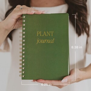 May include: A dark green spiral-bound journal with the text "PLANT journal" in gold lettering on the front cover. The journal measures 8.38 inches in height and 6.25 inches in width, featuring a gold-colored metal wire coil along the left side.