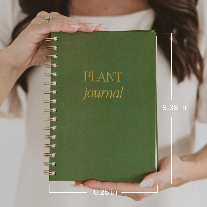 May include: A dark green spiral-bound journal with the text "PLANT journal" in gold lettering on the front cover. The journal measures 8.38 inches in height and 6.25 inches in width, featuring a gold-colored metal wire coil along the left side.