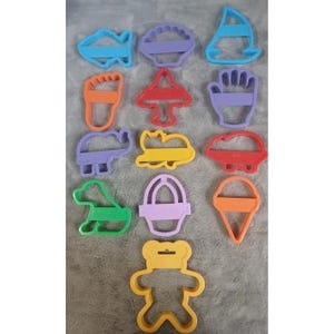 Puede incluir: Un conjunto de cortadores de galletas de plástico de colores en varias formas, incluyendo un pez, un velero, un elefante y un oso de peluche. Los cortadores son en tonos de azul, morado, rojo, naranja, amarillo y verde. Para hornear y manualidades.