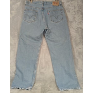May include: Pale blue denim jeans with a classic five-pocket design. The jeans have a straight leg cut and a red Levi's brand tag on the back pocket. The jeans are made of a durable denim material.