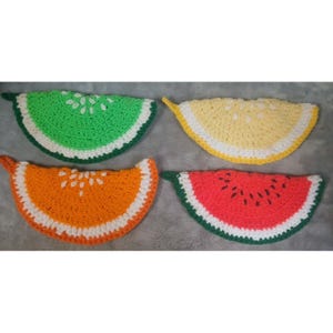 May include: Four crocheted fruit slice-shaped pot holders. The set includes a green lime, yellow lemon, orange, and red watermelon. Each slice has a white rind and seed details. The watermelon has black seed accents.
