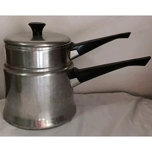 May include: A vintage double boiler pot made of brushed metal with a lid and two black handles. The pot has a classic design, perfect for melting chocolate or preparing delicate sauces. The pot is a light silver color.