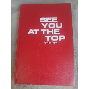 Puede incluir: Un libro rojo con el título "SEE YOU AT THE TOP" en letras mayúsculas blancas. El nombre del autor, "by Zig Ziglar", está impreso debajo. El libro tiene una cubierta texturizada.