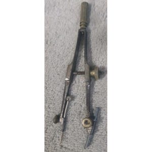 May include: A vintage metal compass with a brass adjustment wheel and a pointed tip. The compass has a ribbed top and a screw for adjusting the width. The tool is designed for drawing circles and arcs.