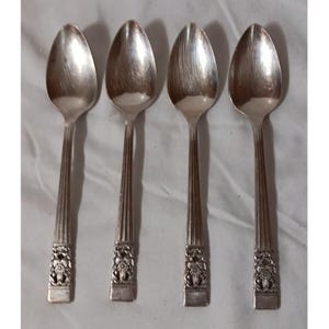 May include: Four silver spoons with a decorative floral design on the handle base. The spoons have a classic, elegant design, with a polished finish. The spoons are arranged side by side on a white surface.