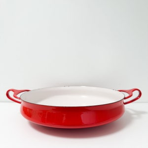 以下が含まれることがあります： 2つのハンドルが付いた赤いエナメル製の鋳鉄製のフライパン。フライパンの内側は白です。