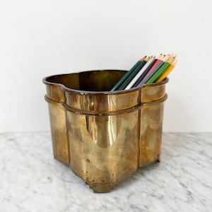 Puede incluir: Un portalápices de latón antiguo con un diseño único de tres secciones. Contiene una colección de lápices de colores. El latón tiene una pátina cálida y envejecida, lo que aumenta su encanto antiguo. El portalápices está sobre una superficie de mármol.