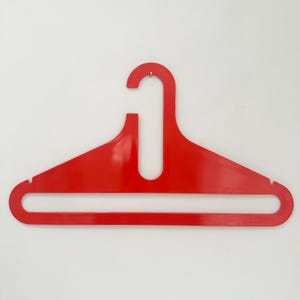 Puede incluir: Una percha roja brillante. La percha está hecha de una sola pieza de plástico moldeado, con un gancho para colgar y una barra horizontal. El diseño es simple y moderno, con un acabado brillante. Para colgar ropa.