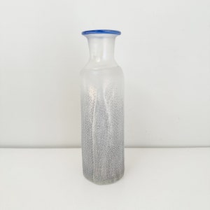 May include: A clear glass vase with a blue rim and a textured pattern. The vase is frosted and has a rectangular shape.