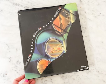 May include: A black box with the words "swatch after swatch" in white and red text. The box features a graphic of a watch face in shades of green, orange, and gold. The word "Electa" is printed in white on the lower right corner.