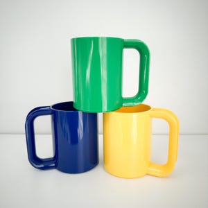 May include: Three plastic mugs in green, blue, and yellow colors. The mugs have large handles and are stacked on top of each other.