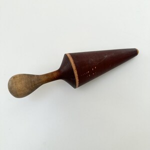 May include: A vintage wooden rolling pin with a dark brown, cone-shaped rolling surface and a light brown handle. The rolling surface is approximately 6 inches long. The handle is rounded. The rolling pin is likely used for baking.