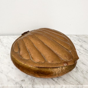 May include: A vintage copper shell-shaped box with a hinged lid. The box is made of hammered copper and has a rustic, antique look.