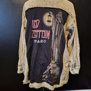 May include: A light green denim jacket with a black back panel featuring the Led Zeppelin logo in red and a graphic of a robed figure holding a lantern. The jacket has long sleeves and a button-down front.