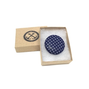 May include: A navy blue fabric button with white polka dots in a small brown box with a white anchor logo.