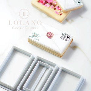 May include: A set of four white cookie cutters shaped like envelopes. The cutters are nested inside each other, with the largest cutter at the bottom and the smallest cutter at the top. The cutters are made of plastic and have a smooth, white finish.