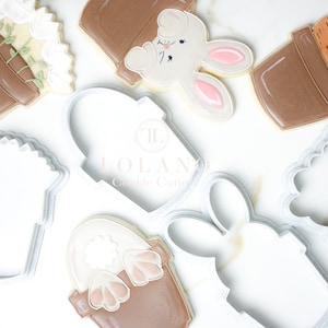 May include: A set of six cookie cutters, including a bunny, a flower pot, and a carrot pot. The cutters are made of white plastic and are designed for making cookies.