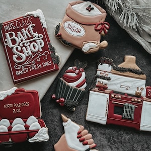Może przedstawiać: Kolekcja ciasteczek o tematyce bożonarodzeniowej. Ciasteczka obejmują czerwony znak z napisem "Mrs. Claus Bake Shop", worek cukru, babeczkę, kuchenkę, karton jajek i dłoń trzymającą worek do dekoracji.