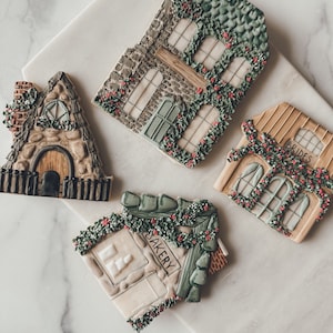 Könnte beinhalten: Vier Lebkuchenhäuser aus Lebkuchen, verziert mit grünem Zuckerguss und roten Streuseln. Die Häuser sind mit "Bakery" und "Brides" beschriftet und haben ein steinartiges Design.