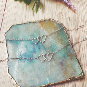 May include: Two silver necklaces with interlocking heart pendants on a teal and gold agate coaster.