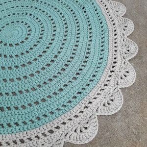 May include: A round crocheted rug with a light blue center and a gray outer border. The border has a scalloped edge.